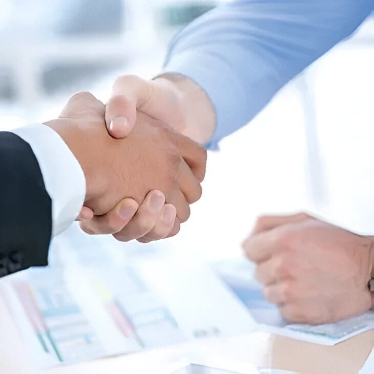 Two people shaking hands over a table.